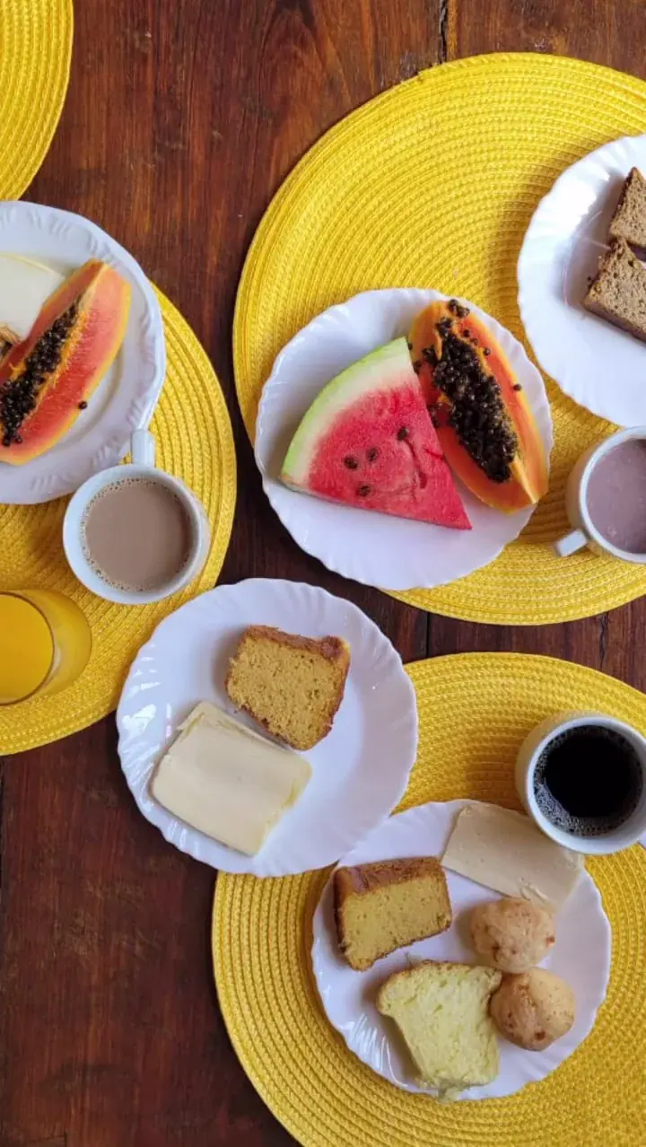 Mesa vista de cima com mamão, melancia, quitandas, bolo, queijo e café