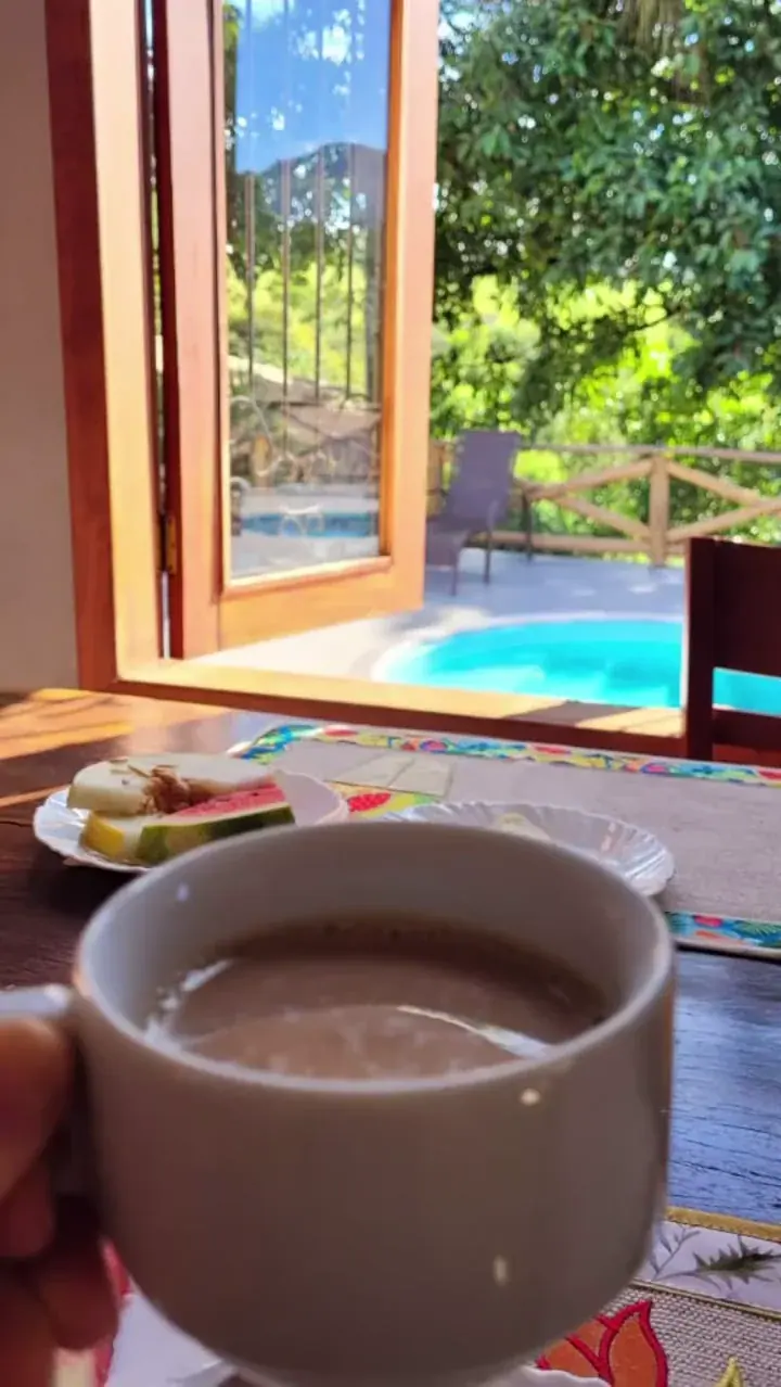 Xícara de café em primeiro plano com a mesa, a piscina e o jardim ao fundo